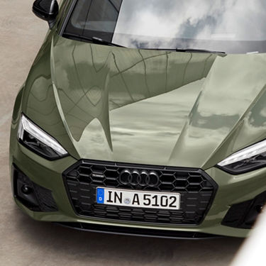 Front view of a green Audi car with European license plate, under a cloudy sky.