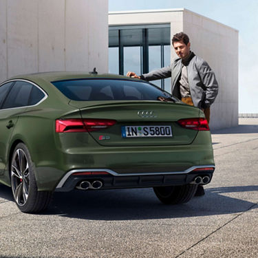 A person standing next to a green Audi S5 Sportback with license plate.