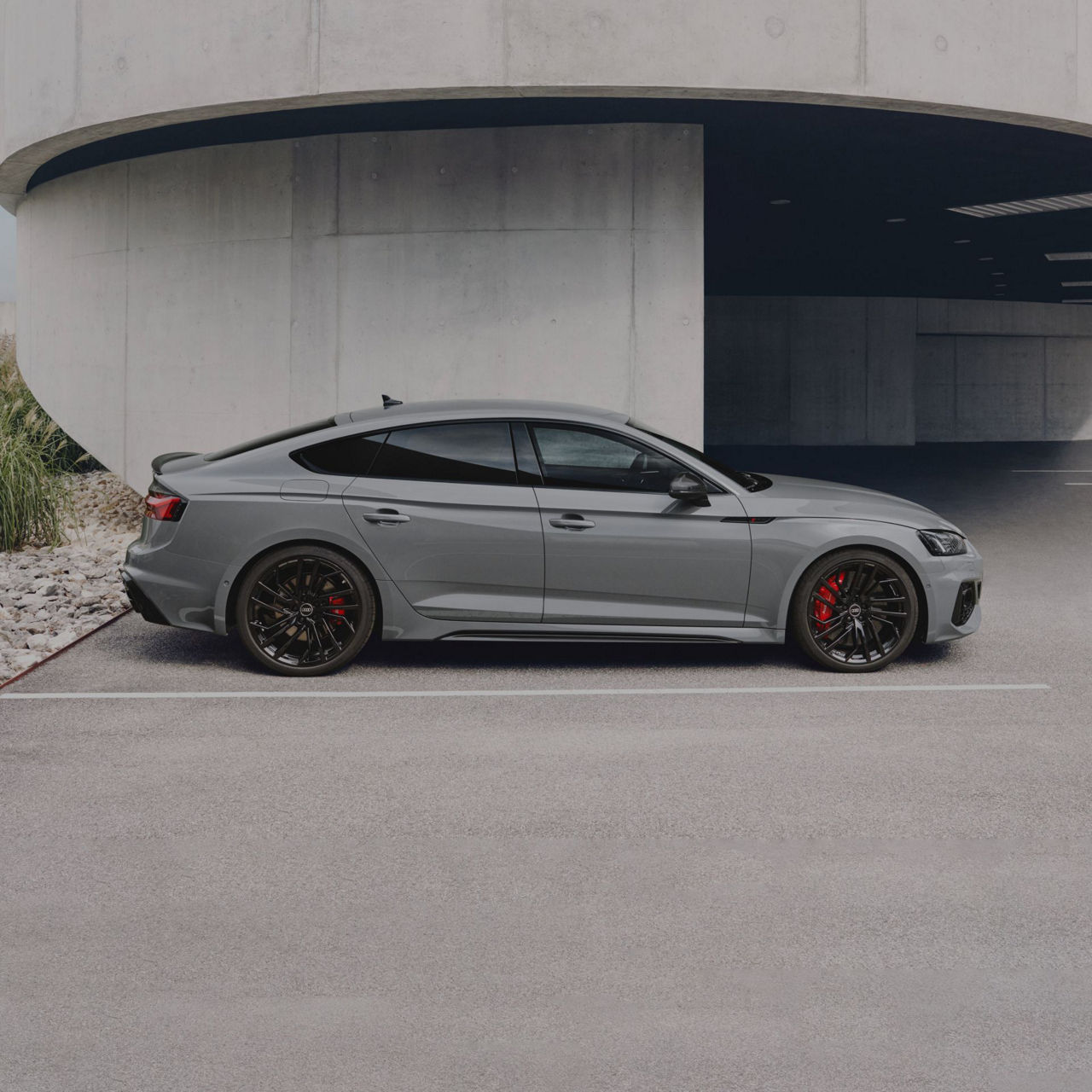 A grey sports sedan parked outside a concrete building, profile view.