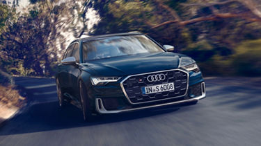 A blue Audi car driving on a road surrounded by blurred trees, indicating speed.