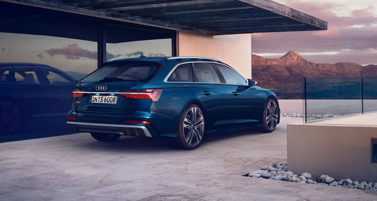 A blue Audi parked near a modern house with mountain views at dusk.