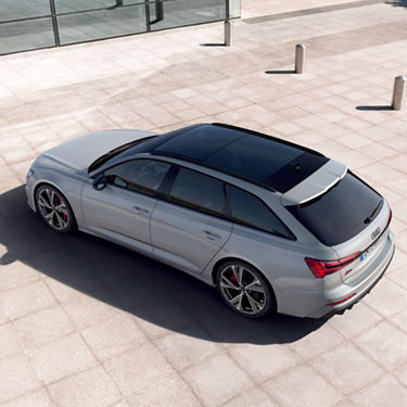 Silver car parked on a paved area near glass building and bollards, captured from above.