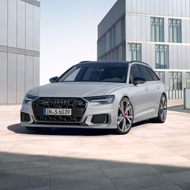Silver Audi parked outside modern building under clear sky.