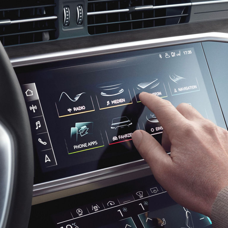 Person interacting with a touchscreen car infotainment system with various icons.