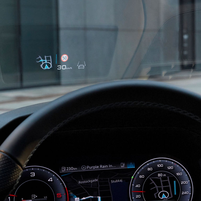 Driver's view of a steering wheel and heads-up display with speed and navigation symbols.