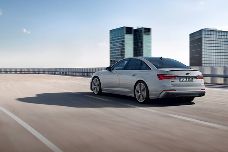 Silver sedan driving on highway with modern buildings in the background.