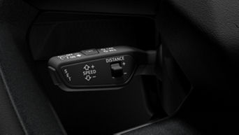 A vehicle's cruise control switch with speed and distance settings, mounted on a black interior.