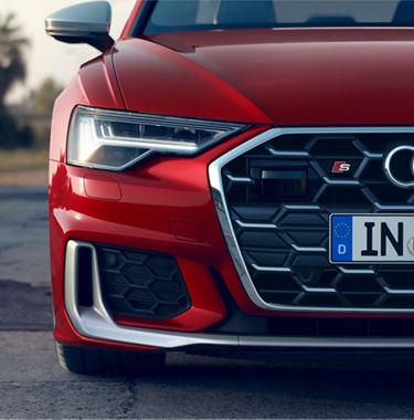 Close-up of a red car's front grille, headlight, and European license plate.