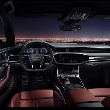 Interior view of a car with dashboard, steering wheel, and city lights through the windshield at night.