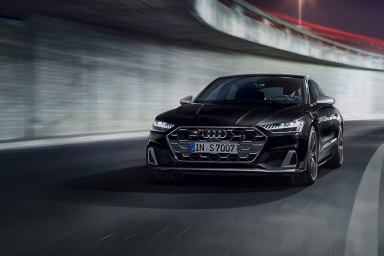 A black Audi car driving on a curved road with motion blur.
