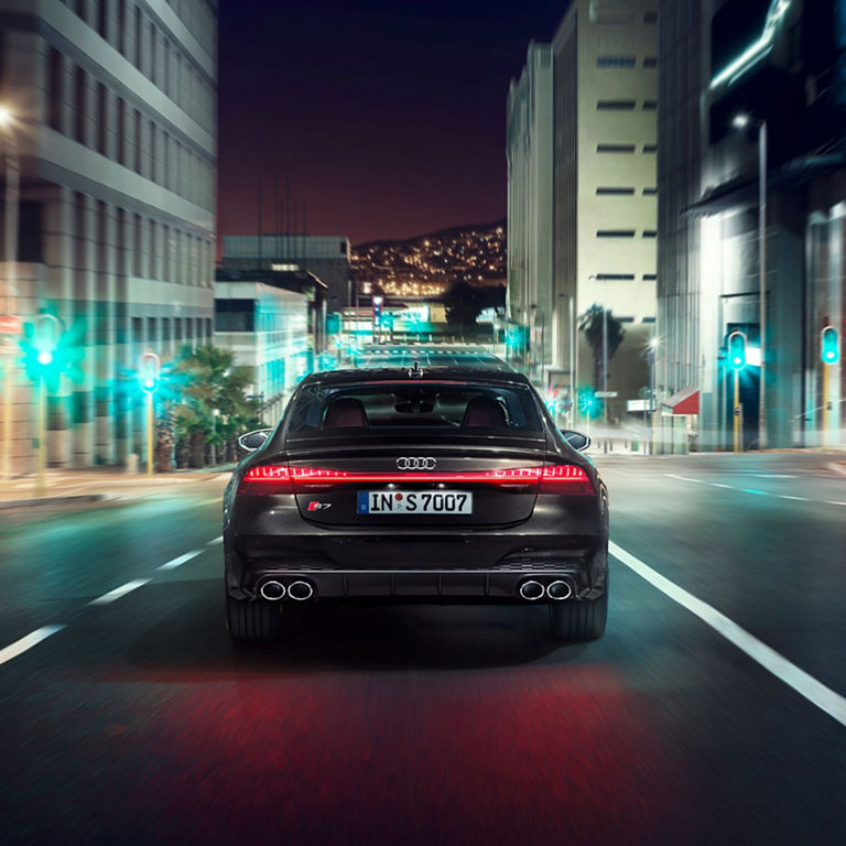 A black sedan driving on a city road with motion blur, near modern buildings.