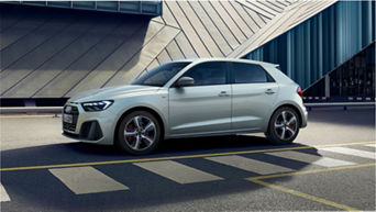 A white Audi hatchback car parked in front of a modern building with geometric patterns.