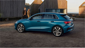 A turquoise hatchback car parked outside modern buildings, near a wooden pier.