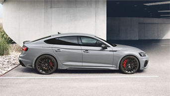 A grey sedan parked near a concrete building under daylight.