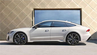 Silver coupe parked by a geometric-patterned wall under clear skies.