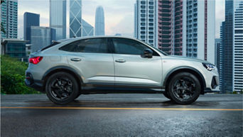 A silver SUV parked on a city street with skyscrapers in the background.