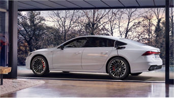 White electric sedan charging in a modern glass-walled garage with trees visible outside.