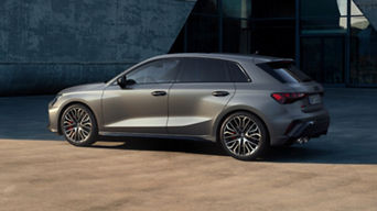 A grey hatchback car parked at an urban location with a concrete building backdrop.