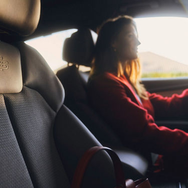 Person in red driving a car, viewed from the passenger seat.
