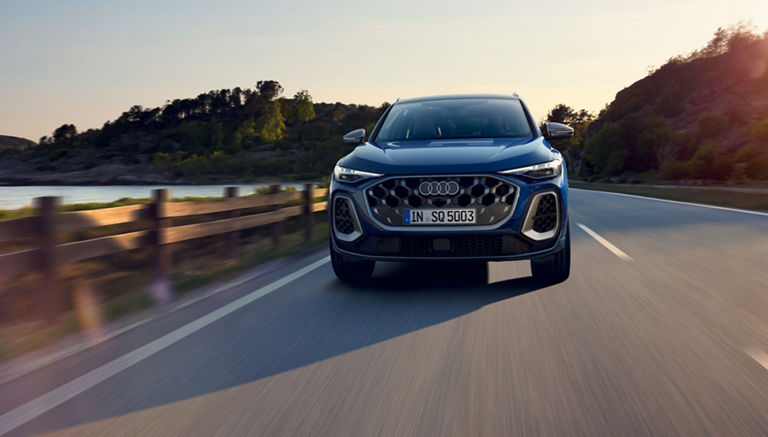 A blue SUV driving on a highway with a scenic backdrop during sunset.