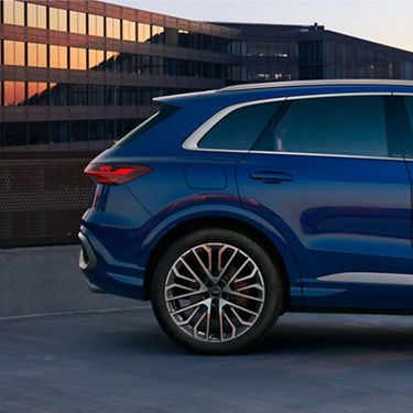 A blue SUV parked in front of a building with reflective windows at dusk.