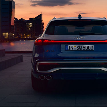 Rear view of an Audi SQ5 on a waterfront at dusk with city skyline.