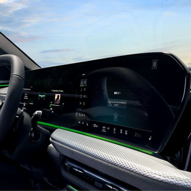 Car dashboard with widescreen digital displays and green ambient lighting.