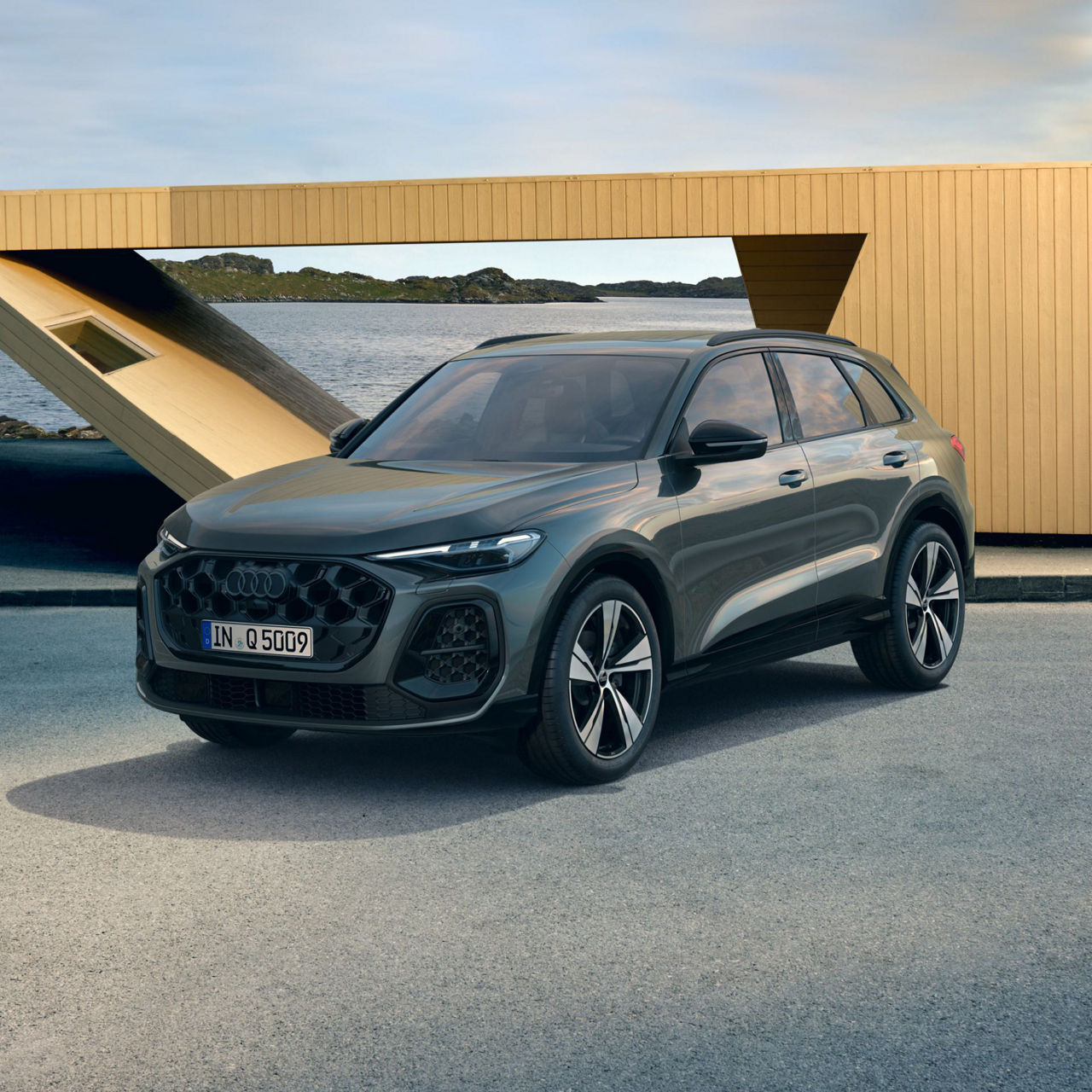 A grey SUV parked by the waterfront with modern architecture in the background.