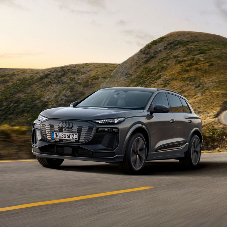 A grey Audi SUV driving on a coastal road with hills in the background.