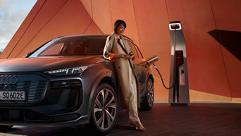 A person in a trench coat charging an electric SUV at a charging station.
