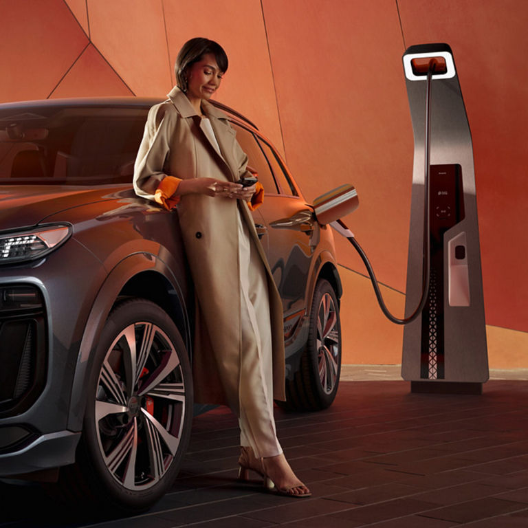 A person in a trench coat charging an electric SUV at a charging station.