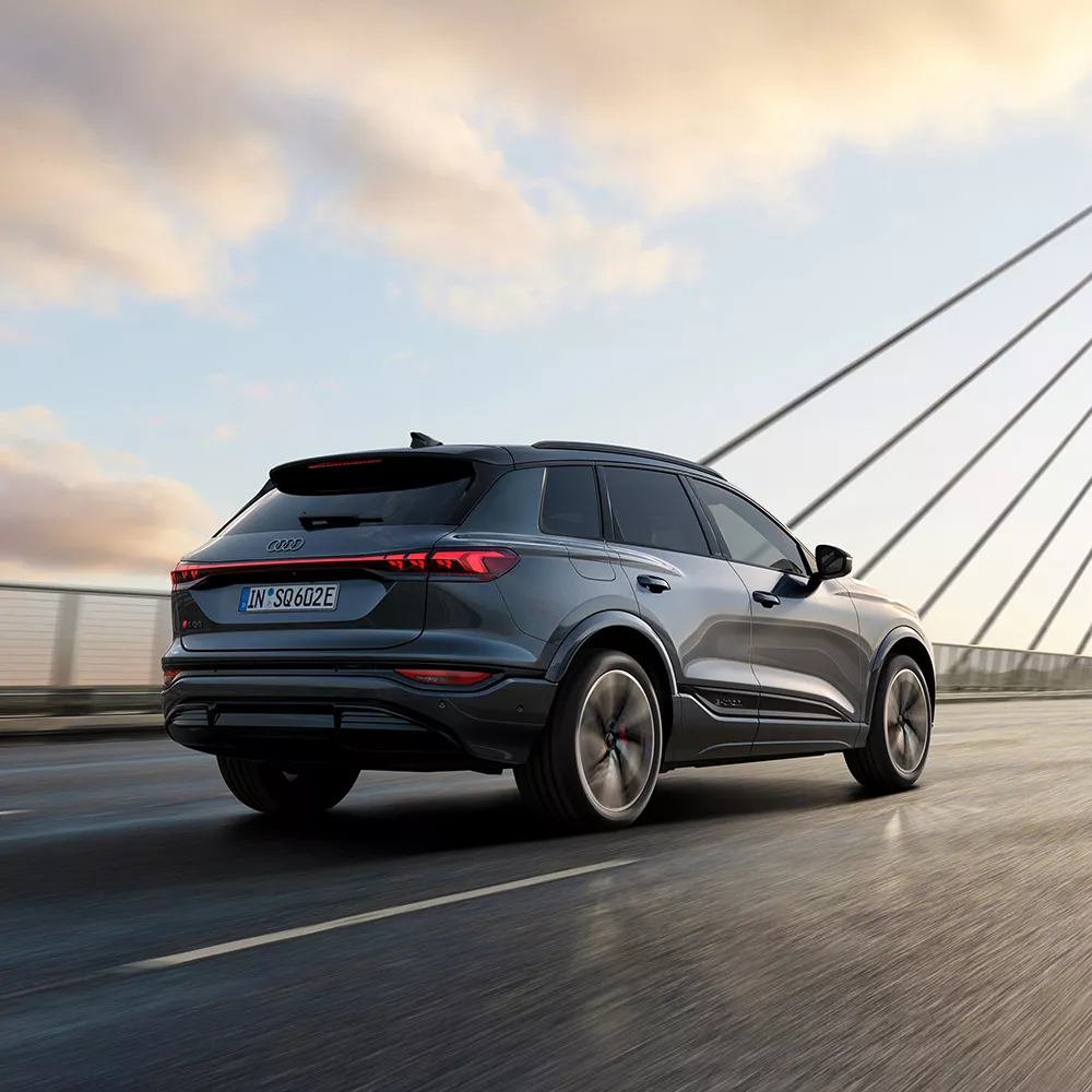 A dark colour SUV driving on a bridge under a cloudy sky.