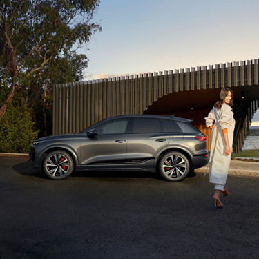 A modern grey SUV parked outside a contemporary building with a person in a white outfit walking past.