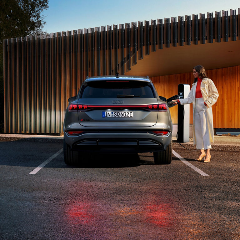 A dark colour SUV charging at an electric vehicle station during sunset.