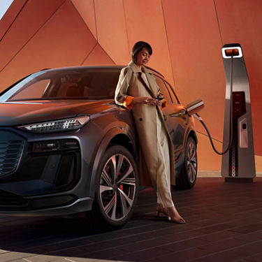 A Audi electric SUV plugged into a charging station with a person standing next to the car.