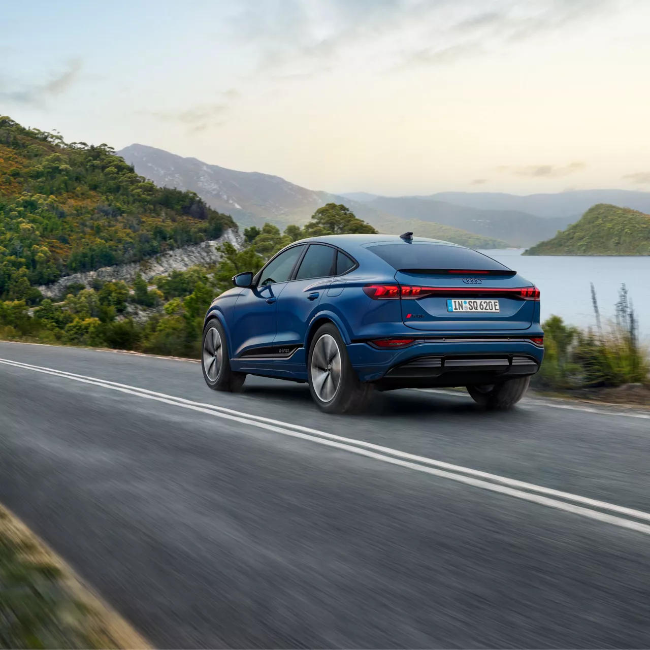 Audi SQ6 e-tron driving alongside a lake with mountains in the back ground.