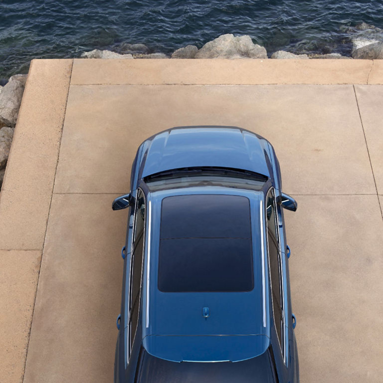 A blue car parked on a pier next to the sea, surrounded by rocks.