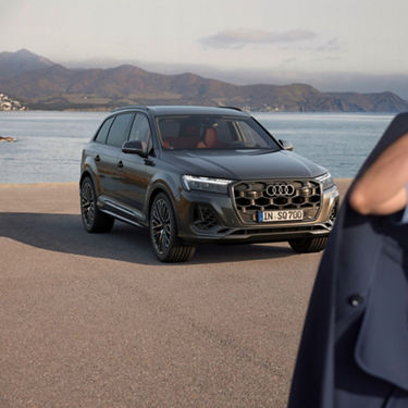 Audi SUV parked by the sea with mountains in the background.