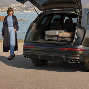 SUV with open trunk by the sea, person nearby, and luggage inside.