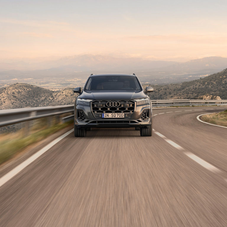 An Audi SUV driving on a winding road with mountains in the background.