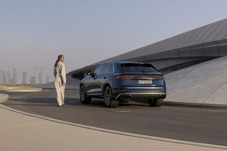 Lady looking over her shoulder at parked Audi SQ8 near modern building.
