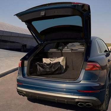  Boot open showing luggage with Audi SQ8 on tarmac near modern building.
