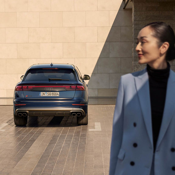 Parked Audi SQ8 facing a styled brick wall with lady looking over her shoulder.