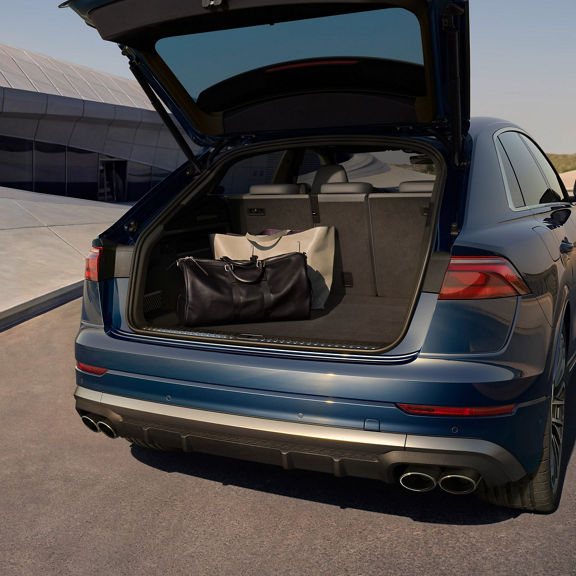 Rear view with open boot of Audi SQ8 on open road next to modern building.