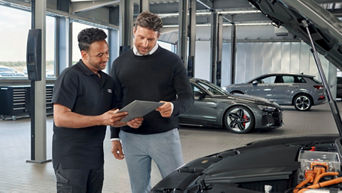 Zwei Männer stehen in einer Werkstatt mit Audis und schauen auf ein IPad