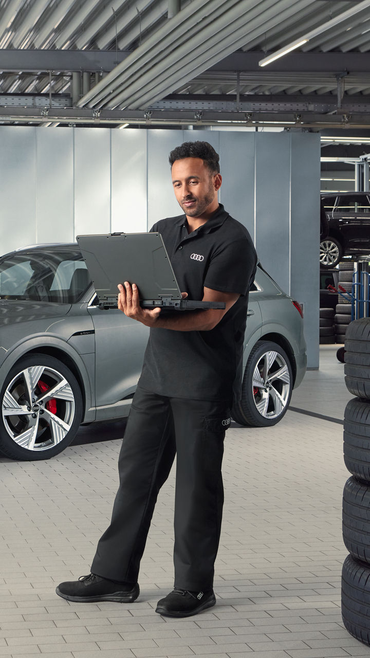 Mann steht mit einem Tablet in einer Werkstatt, vor einem Audi