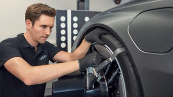 Mann mit Handschuhen verrichtet Arbeiten an einem Reifen eines Audi