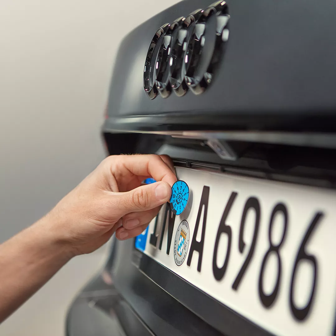 Eine Hand klebt eine HU-Plakette an ein Kennzeichen