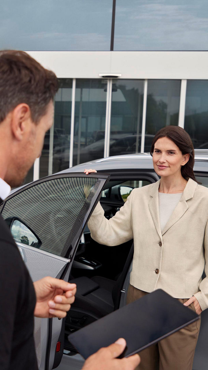 Mann spricht mit einer Frau, die vor einer geöffneten Tür eines Audi steht