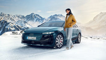 Frau steht neben einem grünen Audi S6 Sportback e-tron vor verschneiter Bergkulisse.